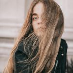 Portrait of a young woman with long hair in the wind, wearing a leather jacket outdoors.